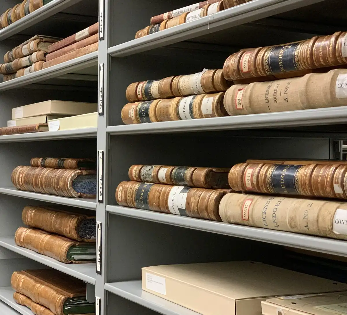 Metal archive shelves holding rows of old leather-bound record books with paper labels