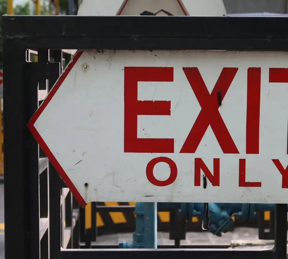 A red and white Exit Only sign with an arrow, mounted on a railing