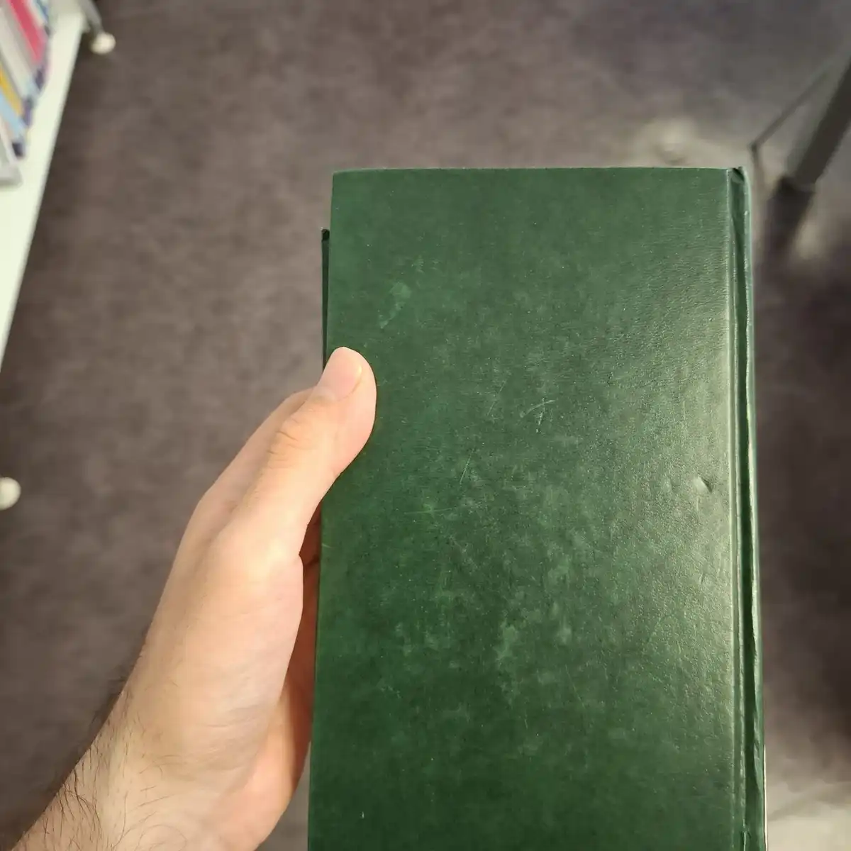 A hand holding a plain dark green hardcover book