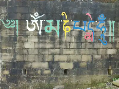 Colorful Tibetan script painted along the top of a weathered brick wall