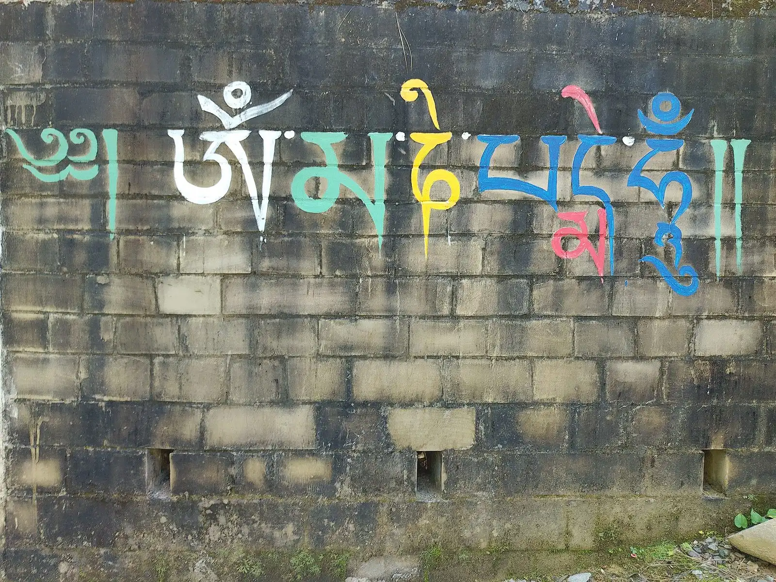 Colorful Tibetan script painted along the top of a weathered brick wall