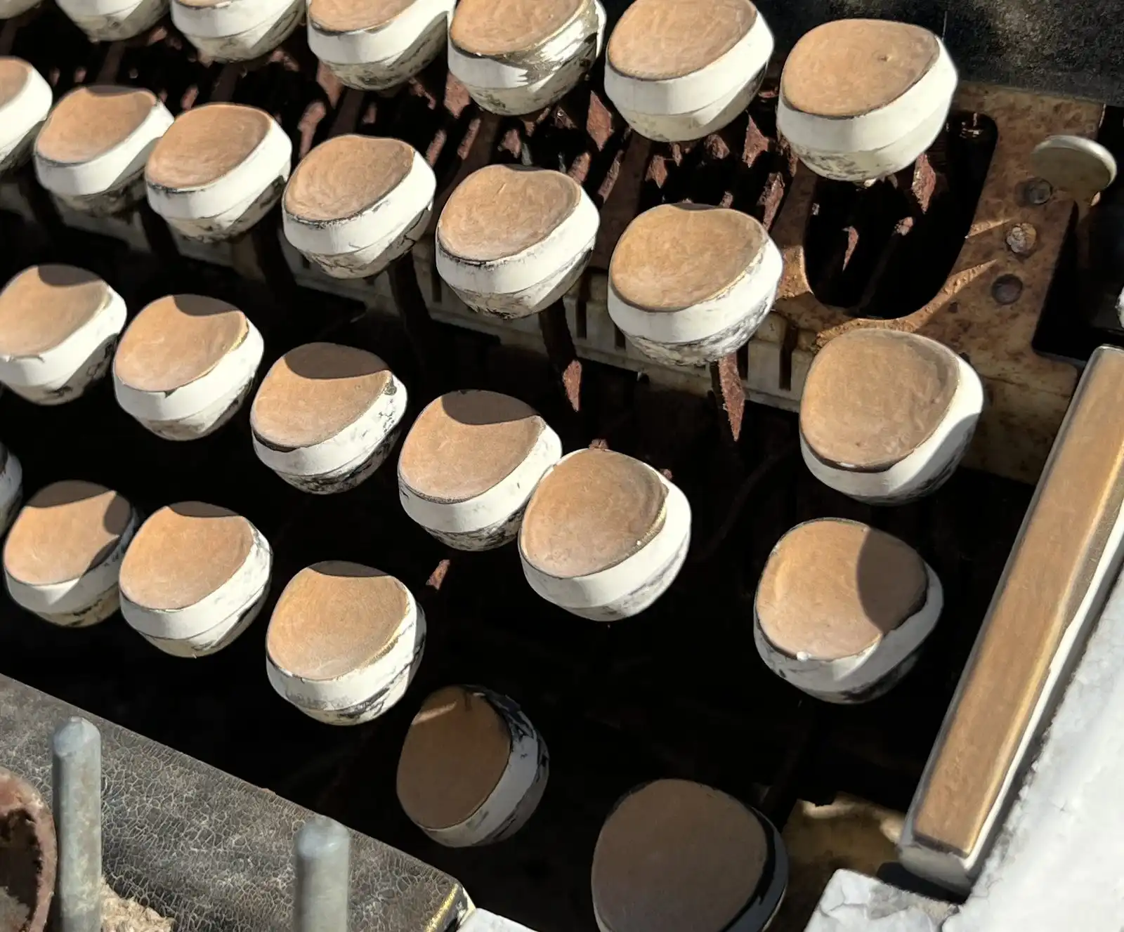 Rows of round, worn typewriter keys painted white, on an old machine standing outdoors in the sun