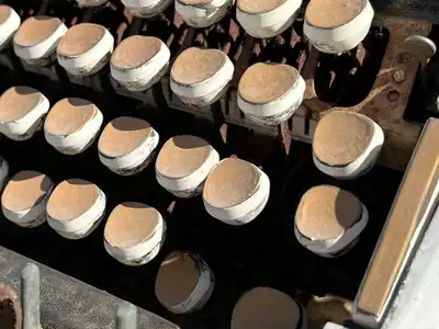 Rows of round, worn typewriter keys painted white, on an old machine standing outdoors in the sun